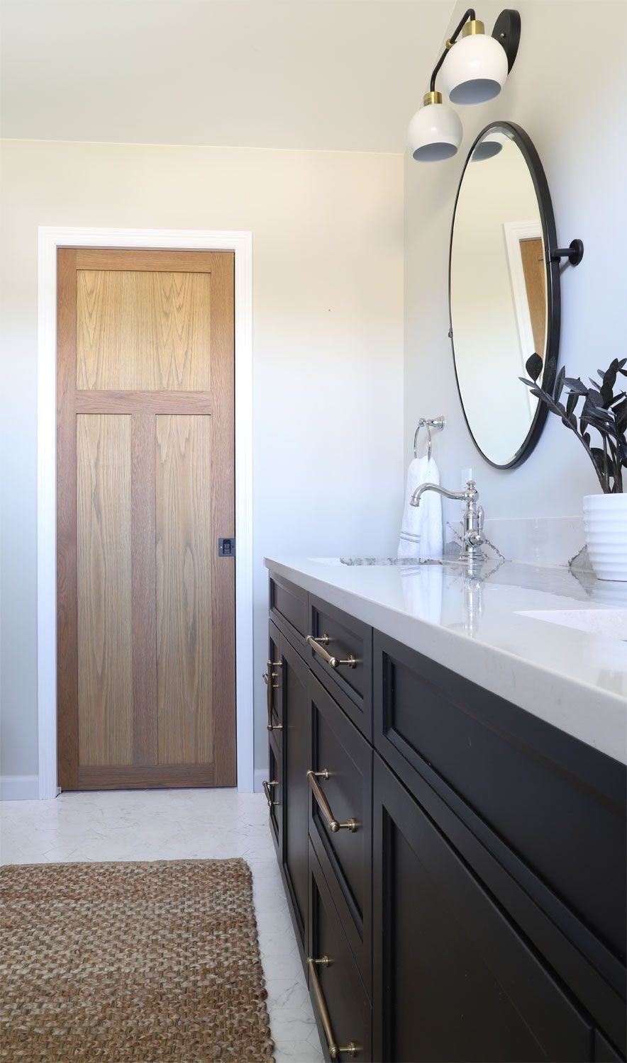 A bathroom with a wooden door , black cabinets , a sink and a mirror.