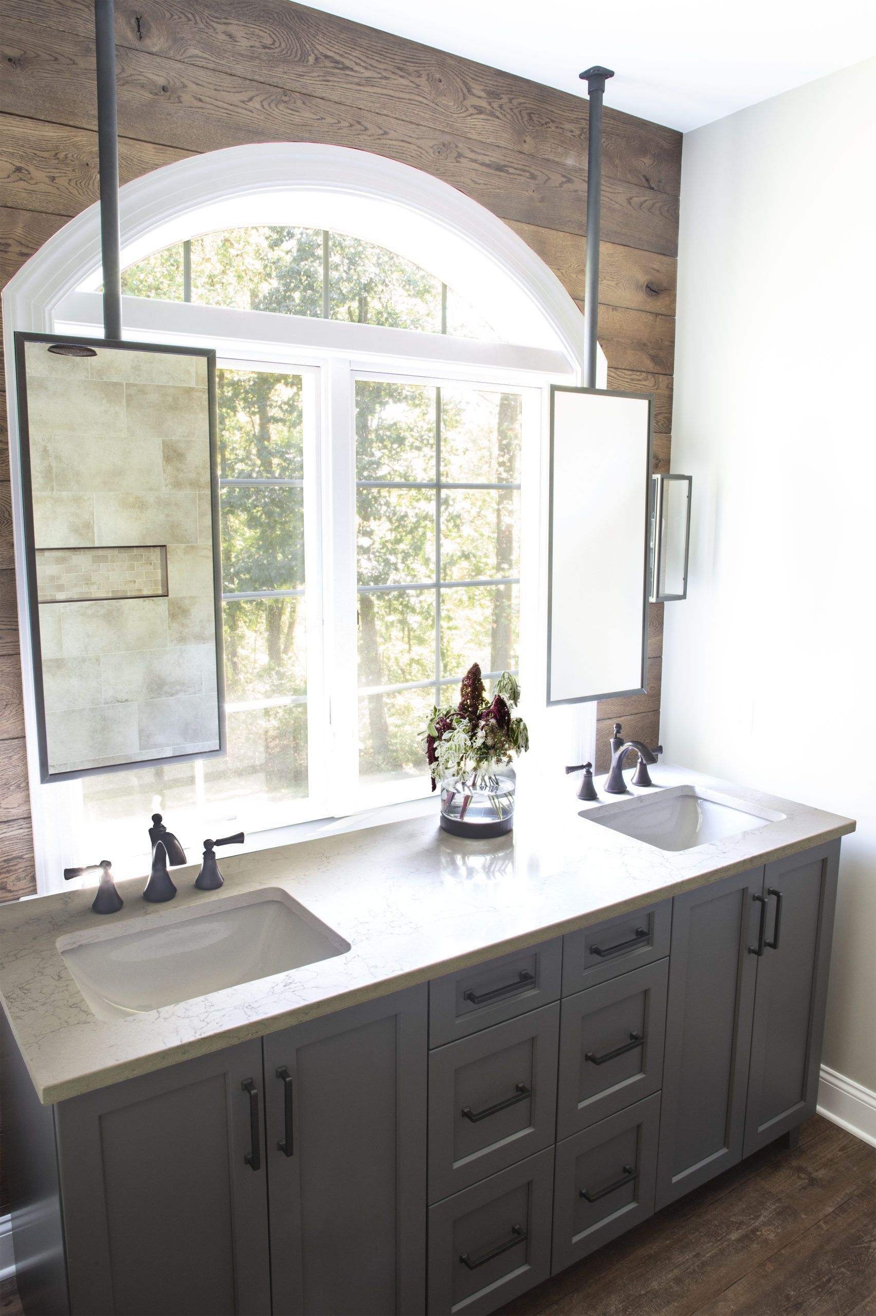 A bathroom with a sink and two mirrors hanging from the ceiling.
