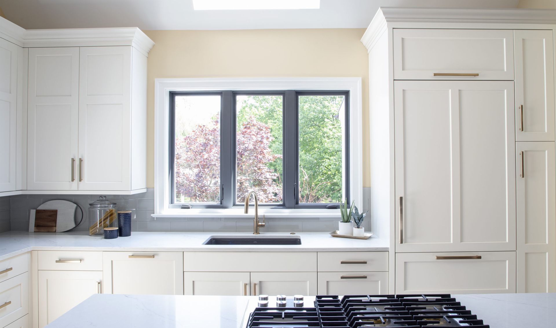 A kitchen with white cabinets , a stove , a sink and a window.