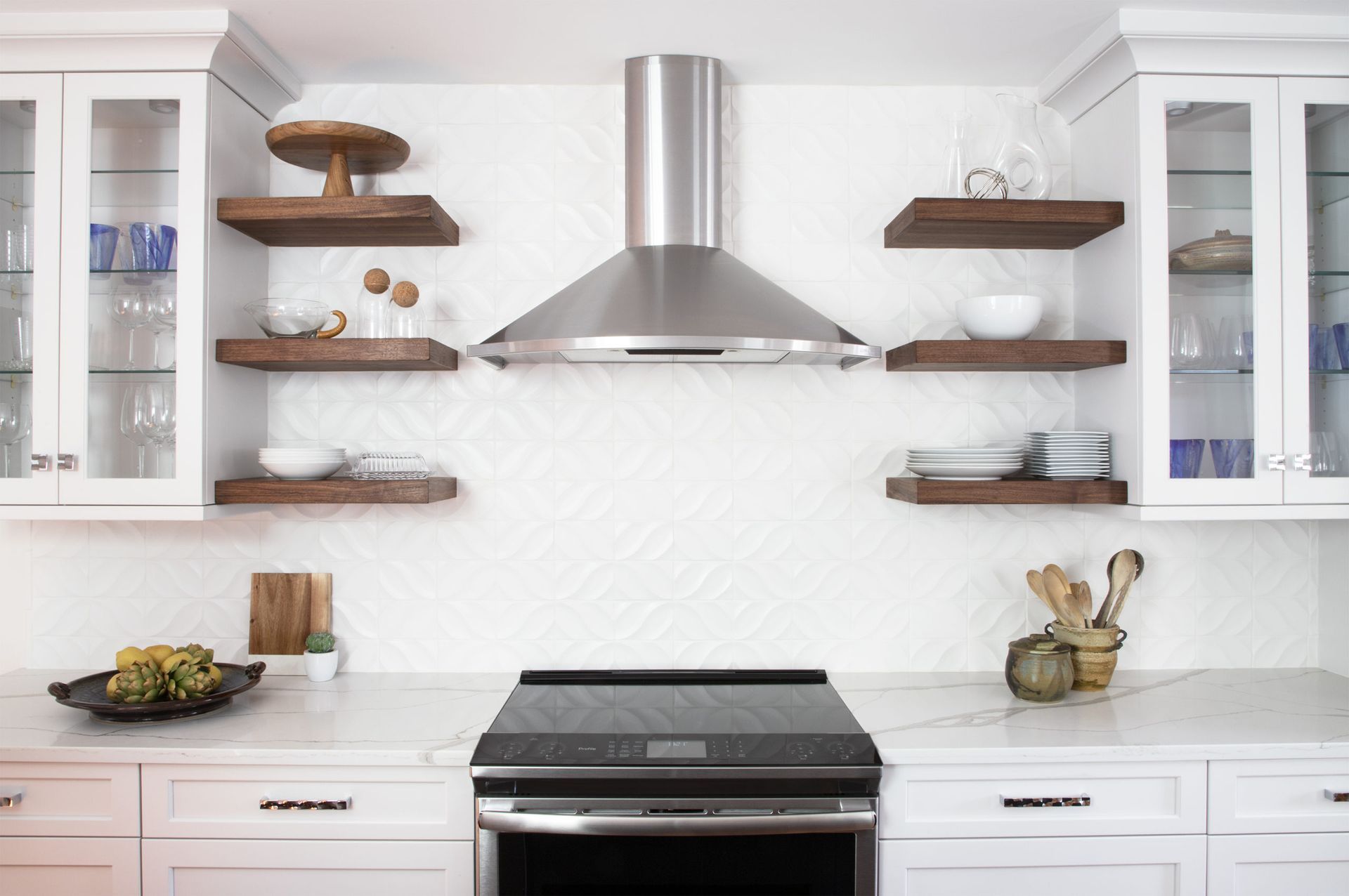 A kitchen with a stove , oven , shelves and a hood.