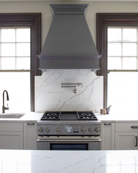 A kitchen with a stove , sink , and hood.