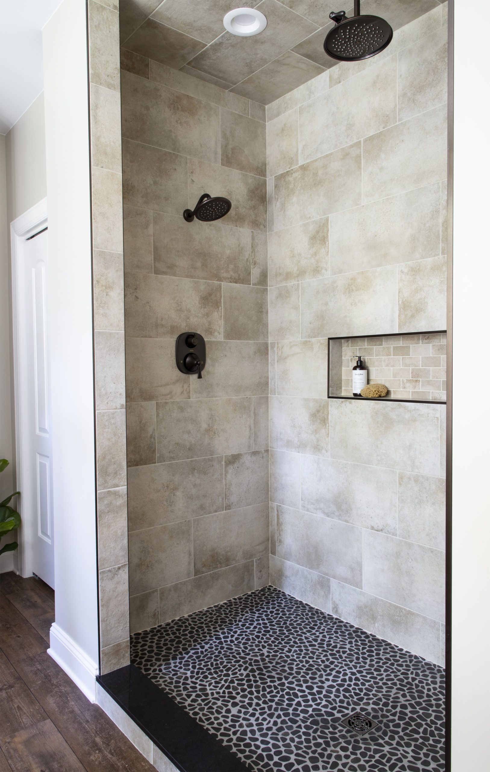 A walk in shower with two shower heads and a shelf.
