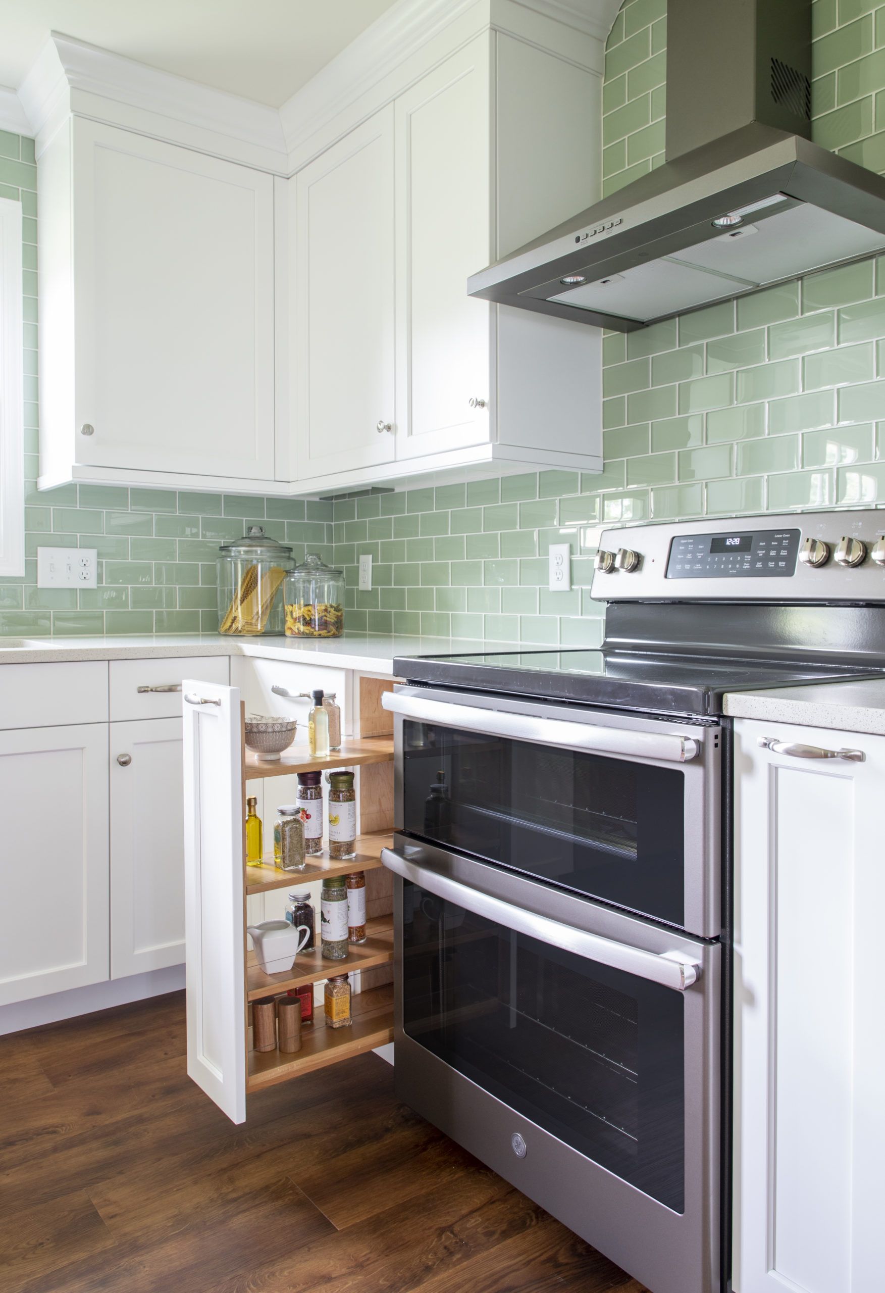 A kitchen with a stove , oven , cabinets and a pull out spice rack.