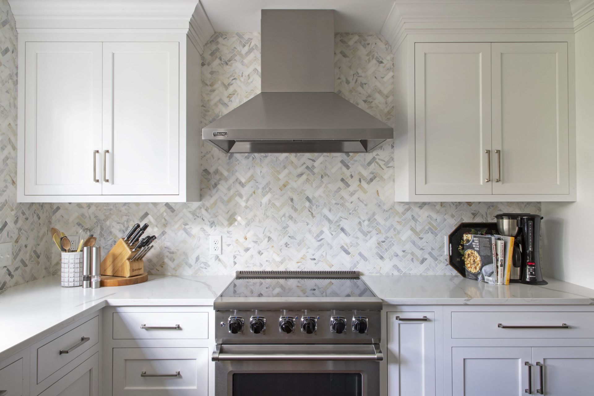A kitchen with white cabinets , a stove , and a hood.