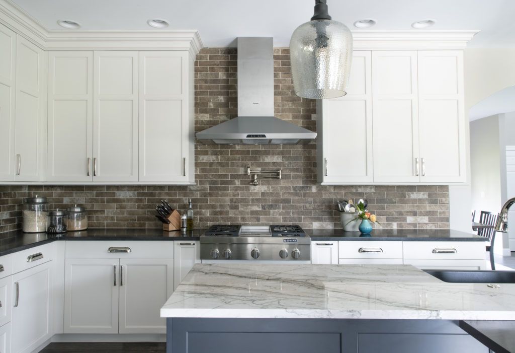 A kitchen with white cabinets , black counter tops , a stove and a sink.