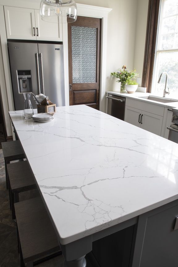 A kitchen with a large white counter top and a stainless steel refrigerator.