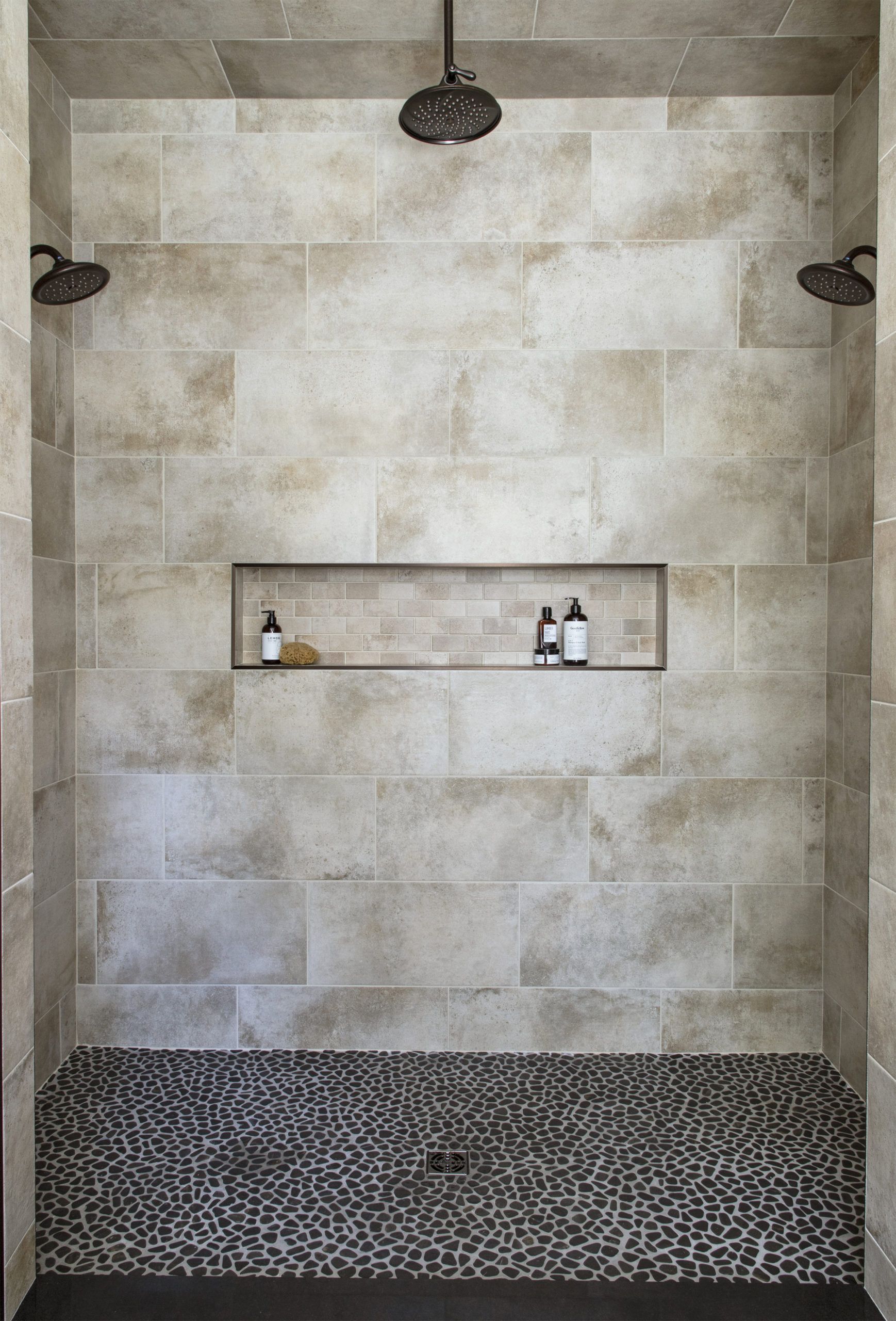 A shower with two shower heads and a shelf with bottles on it.