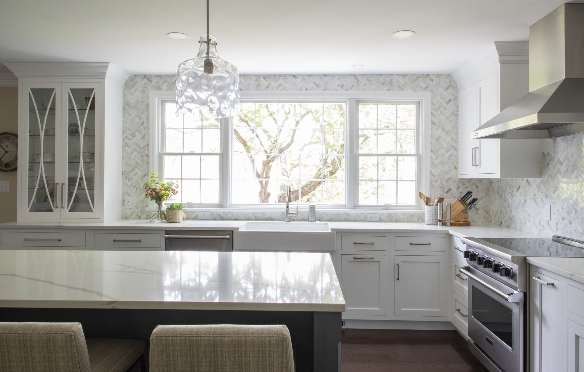 A kitchen with white cabinets , stainless steel appliances , a large island , and a large window.