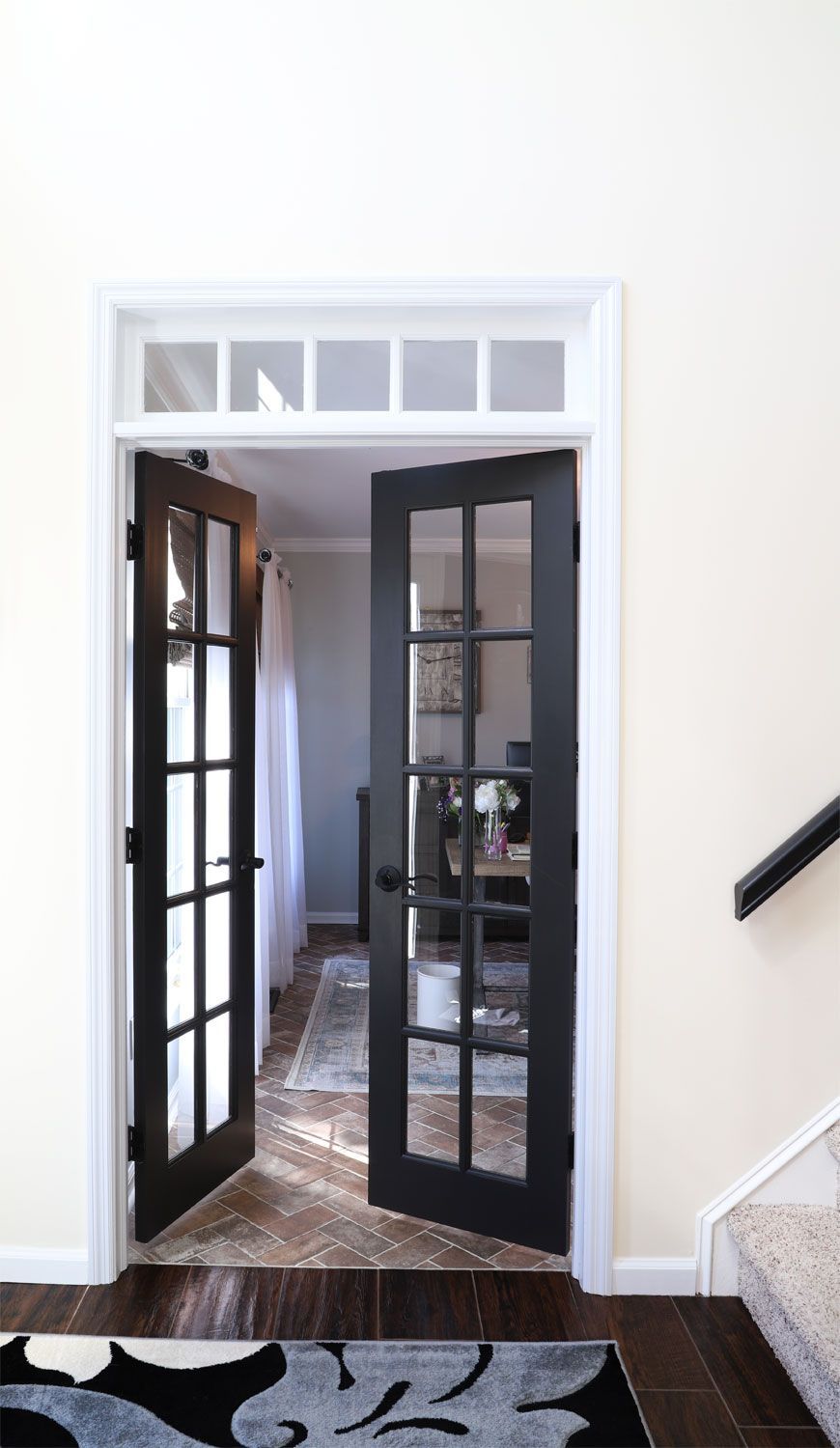 A pair of black french doors are open to a living room.