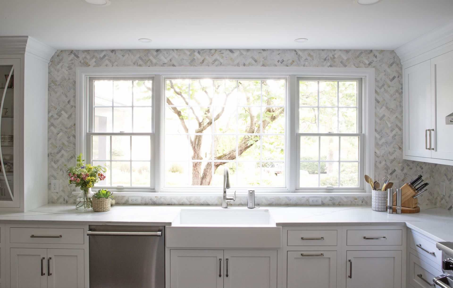 A kitchen with white cabinets , stainless steel appliances , a sink and a large window.