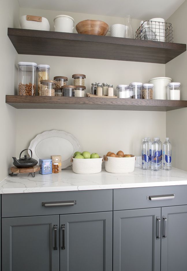 A kitchen with gray cabinets and wooden shelves filled with food and drinks.