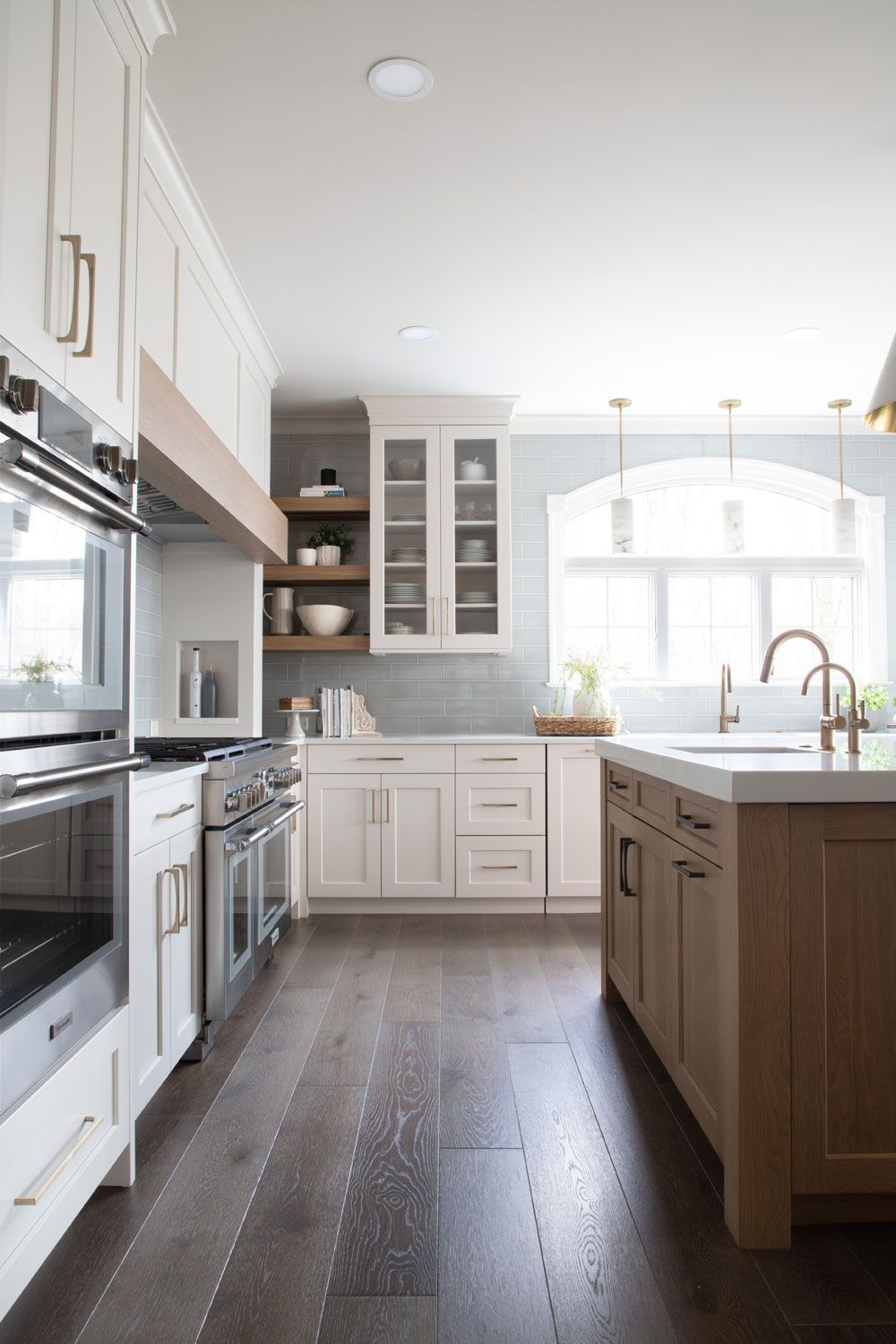 A kitchen with white cabinets , wooden floors , stainless steel appliances and a large island.