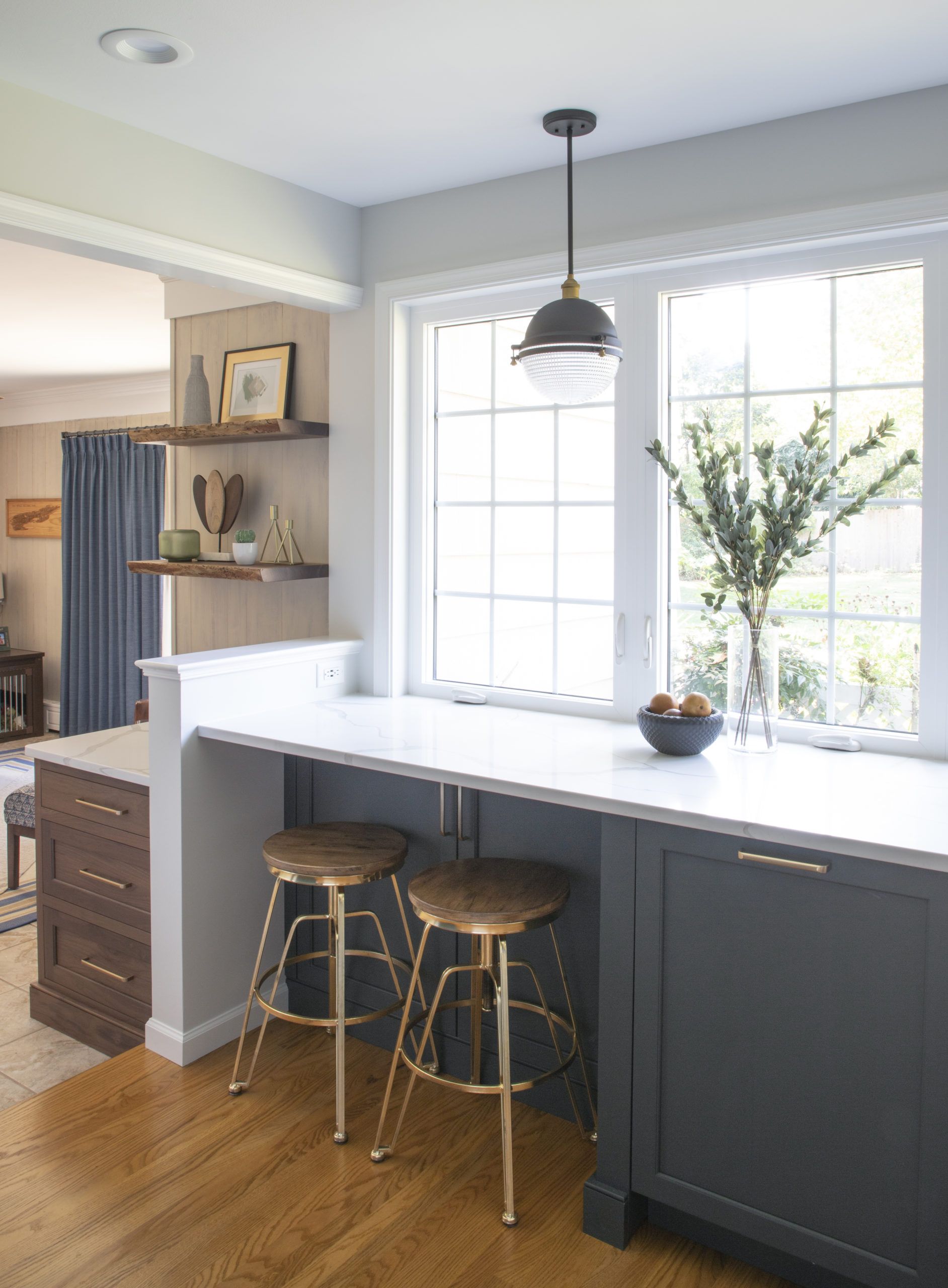 A kitchen with a long counter and stools next to a window.