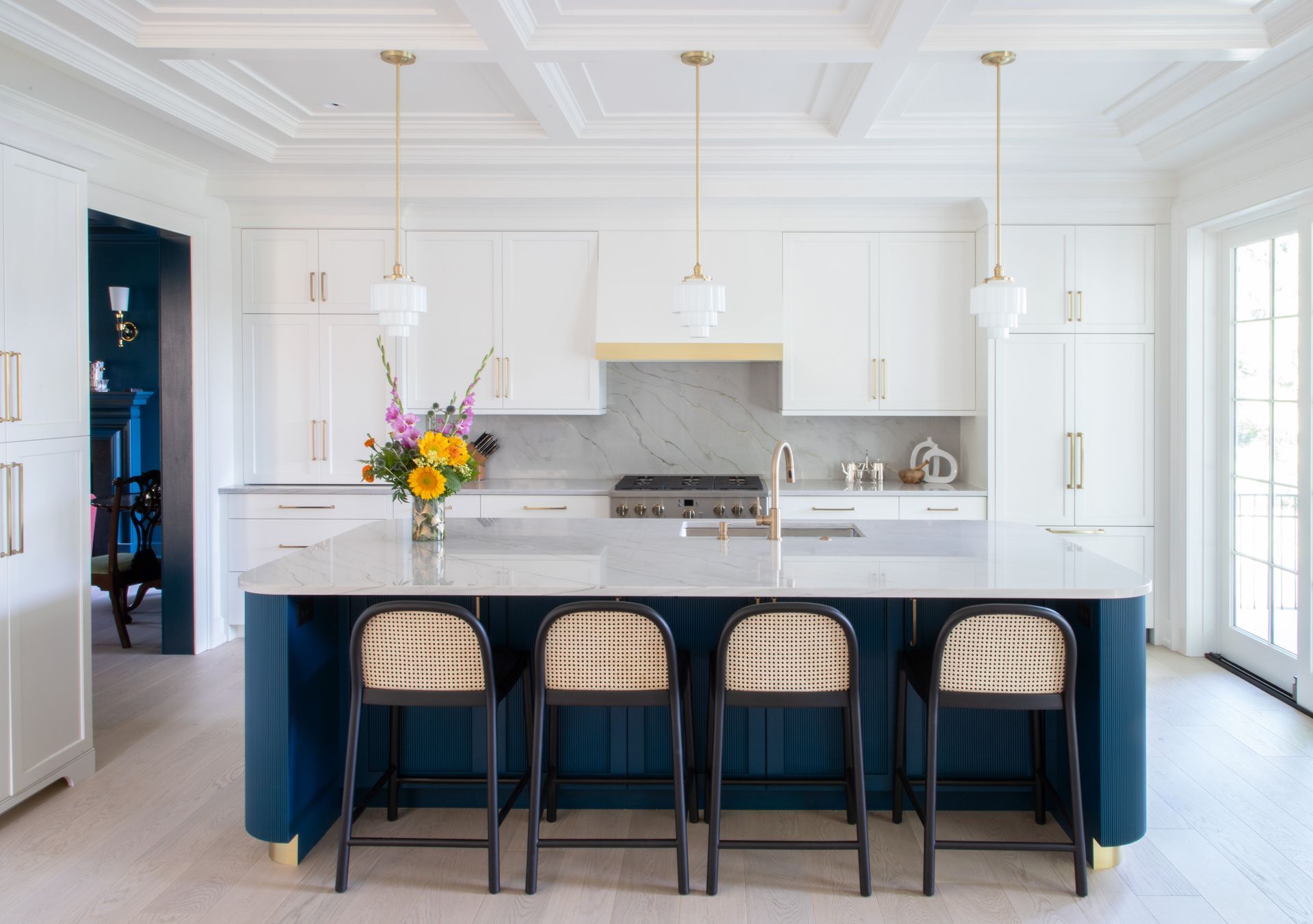Blue and white kitchen with island seating, gold accents, and floral arrangement.