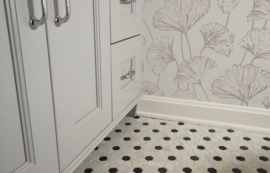 A bathroom with white cabinets and a black and white tile floor.