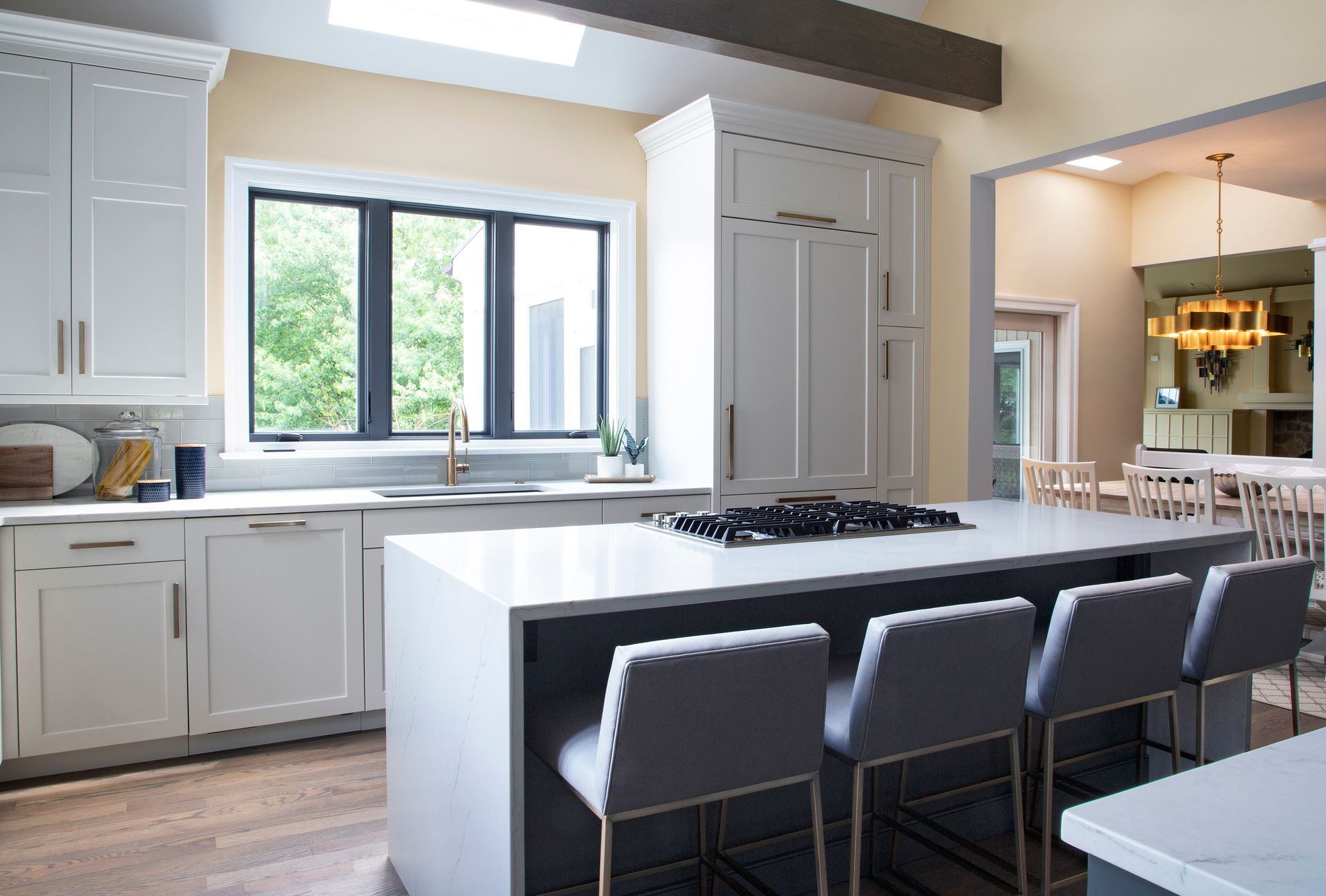 White kitchen with marble countertops, range, and sink by a window. Island with dark brown cabinetry.