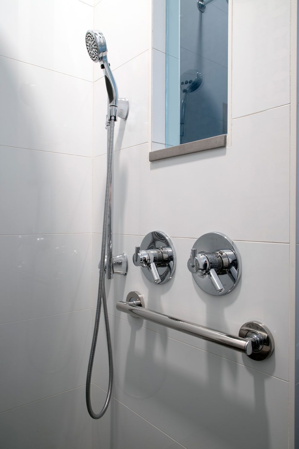 An ADA complaint bathroom shower with a hand rail and a mirror on the wall.
