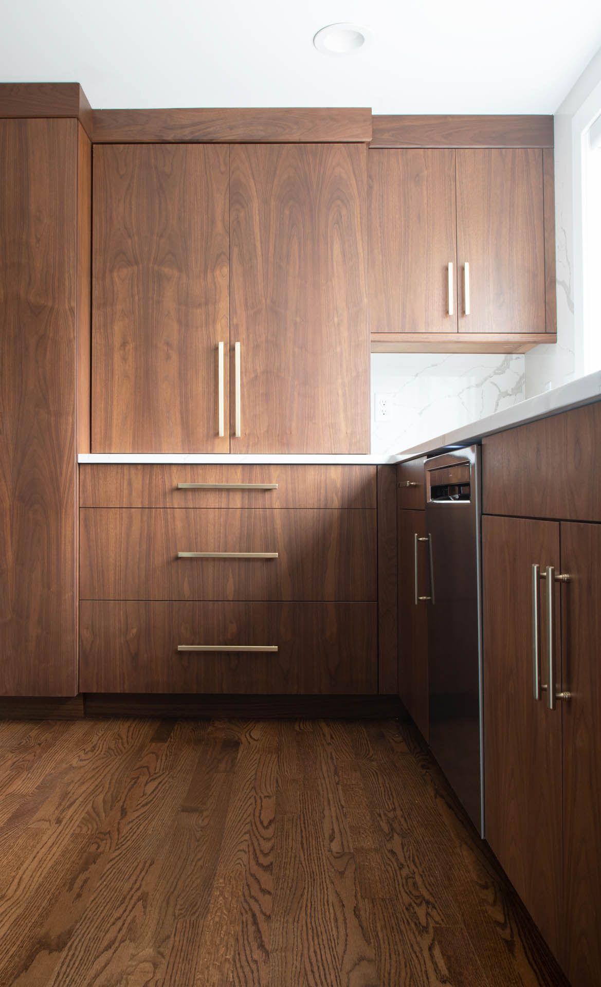 A modern kitchen featuring rich, dark wood grain cabinets, stainless steel hardware, and light wood flooring.