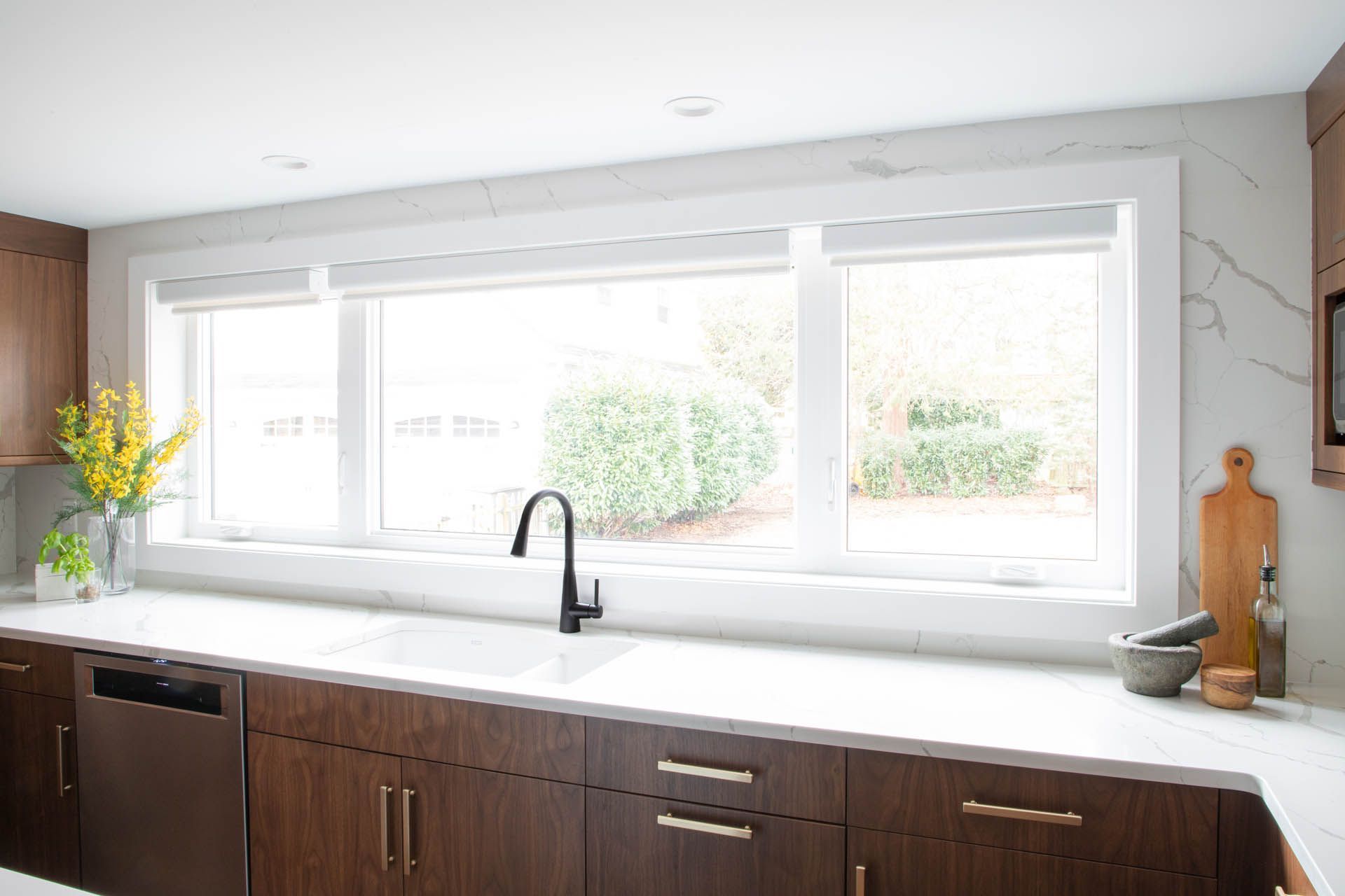 Modern kitchen sink area with a white countertop, dark wood cabinets, a black faucet, and a large window.