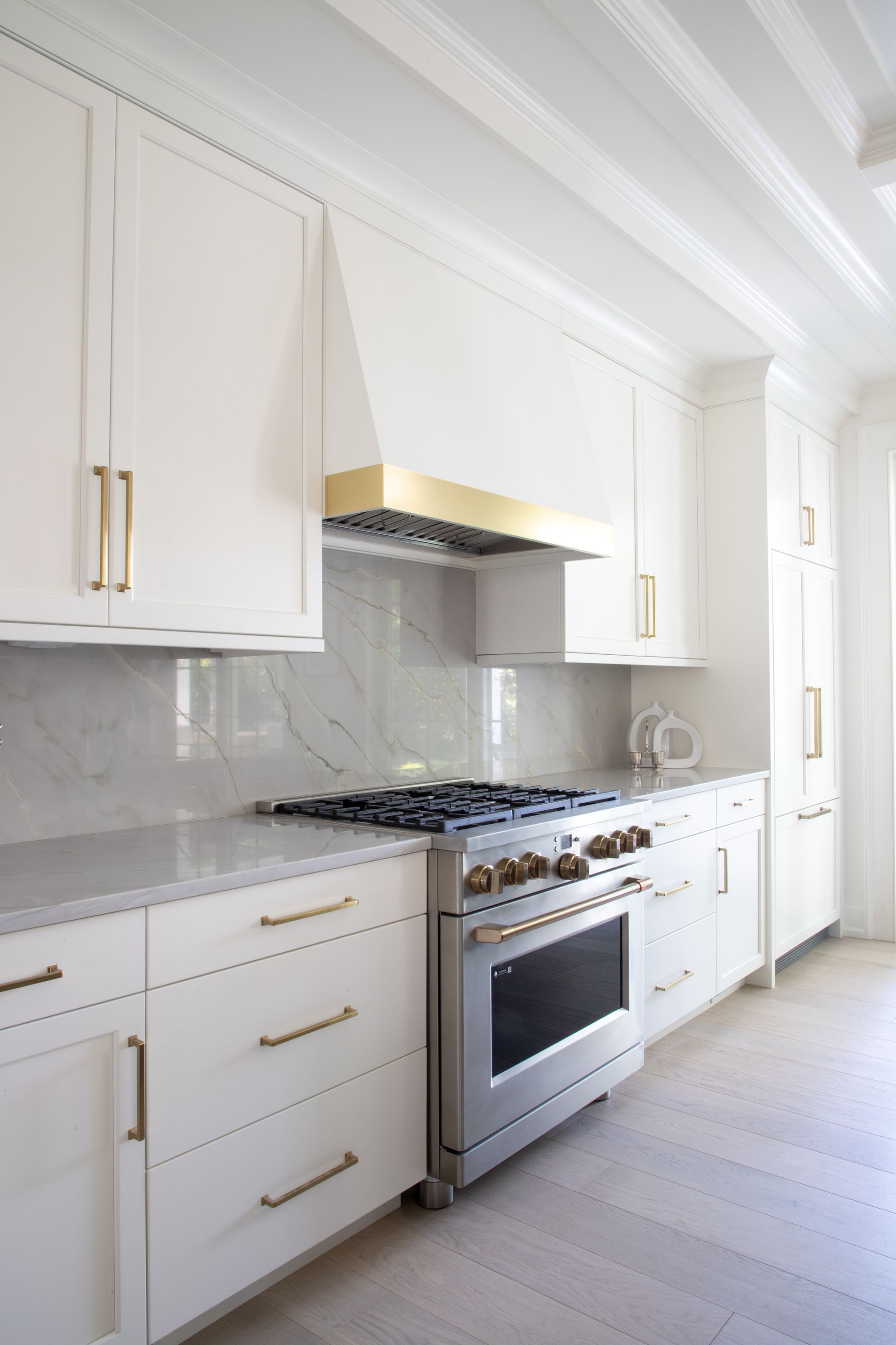 White kitchen with gold accents. Stainless steel range and hood.