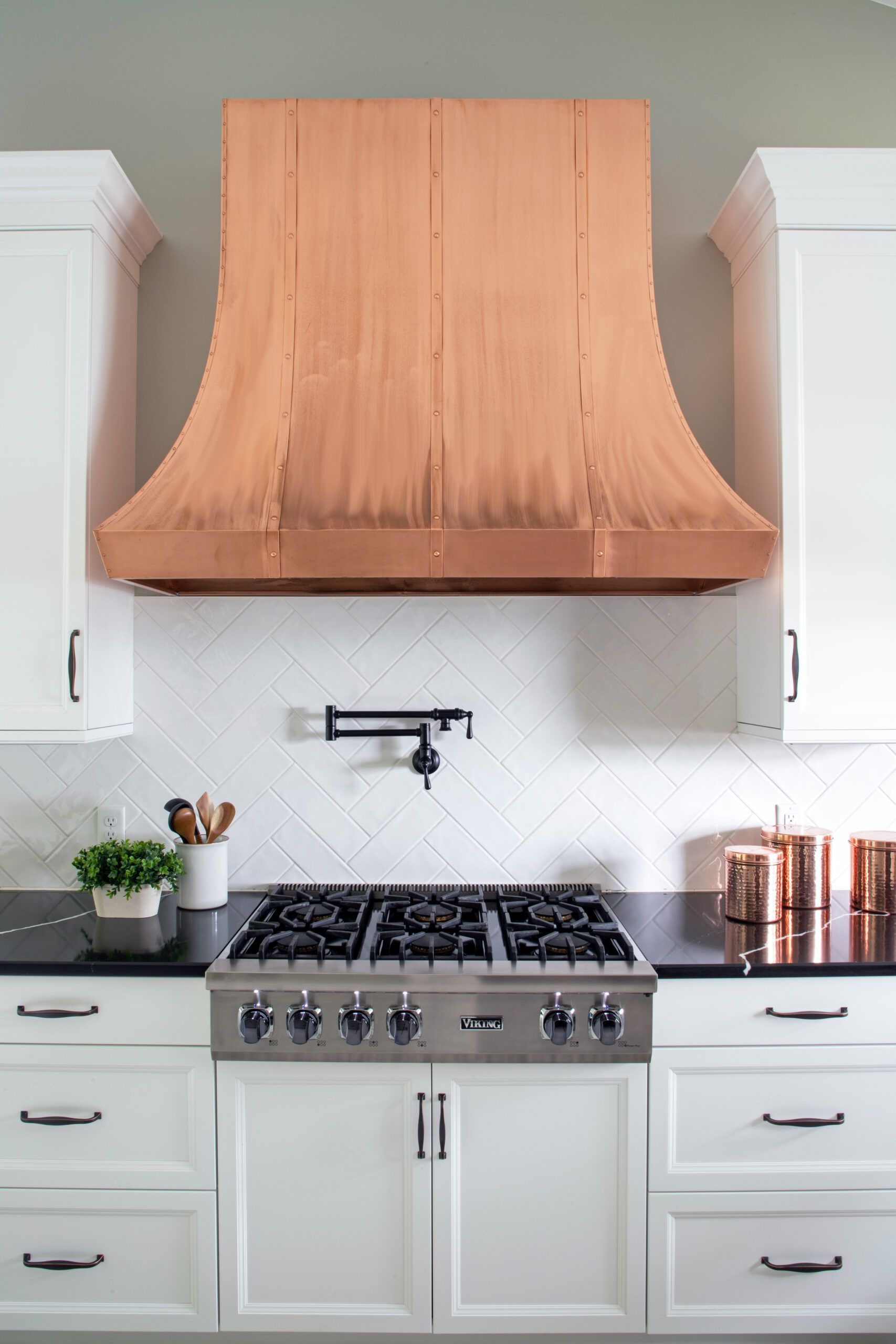 A kitchen with white cabinets and a copper hood over the stove.