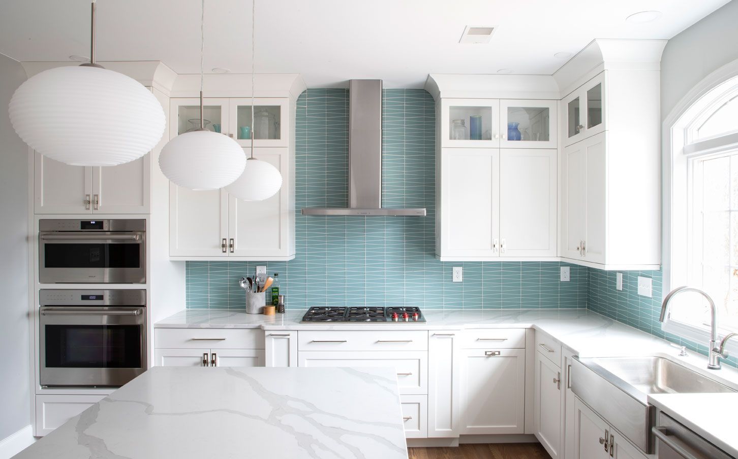 A kitchen with white cabinets , blue tiles , stainless steel appliances and a large island.