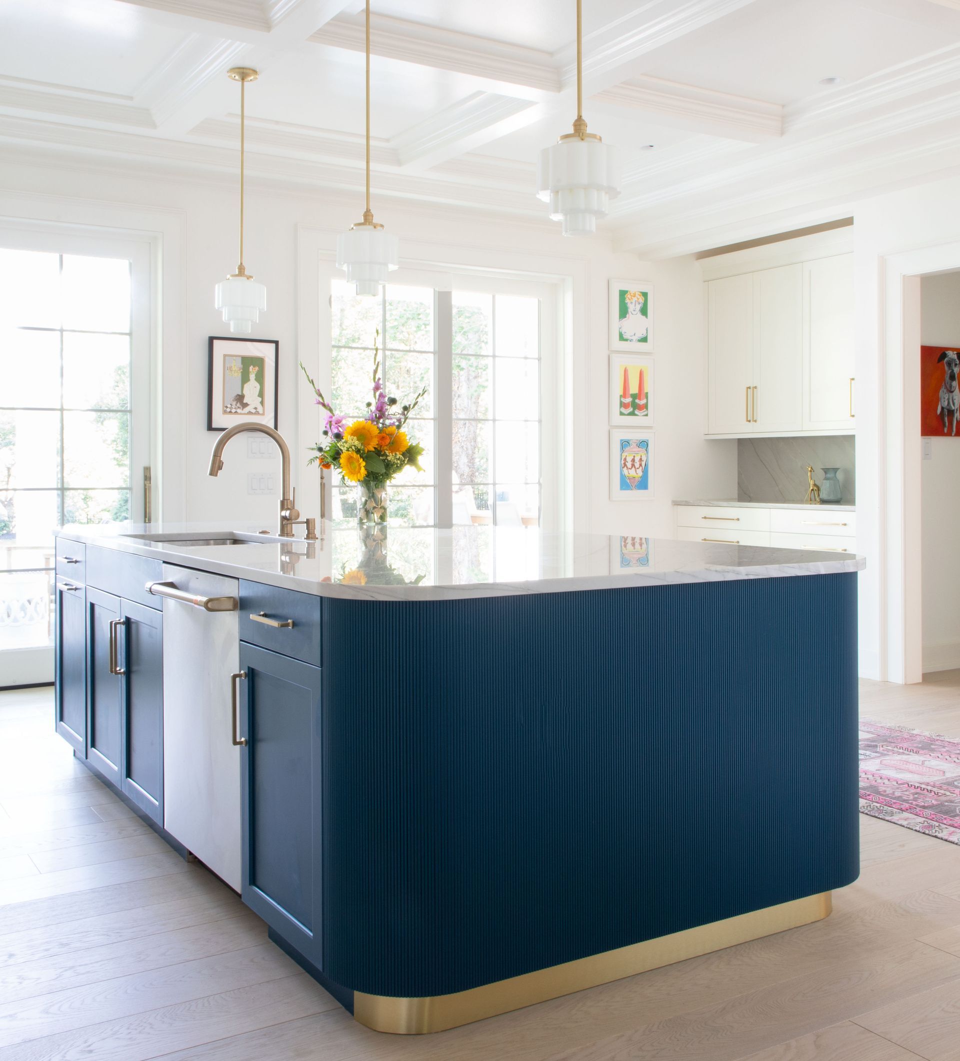 Blue kitchen island with gold trim, white countertop, pendant lights, and white cabinets.