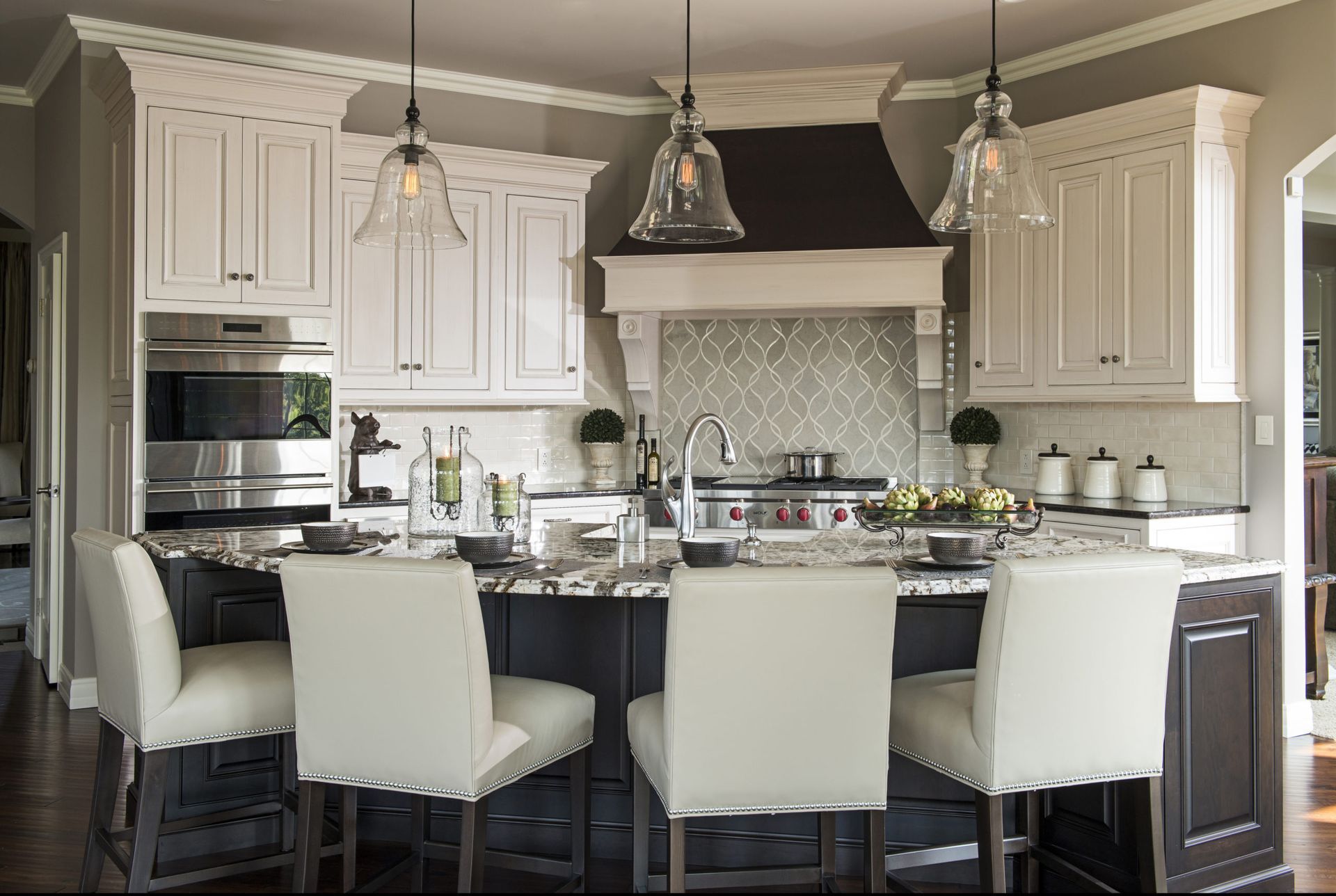 A kitchen with white cabinets , black counter tops , stainless steel appliances and a large island.