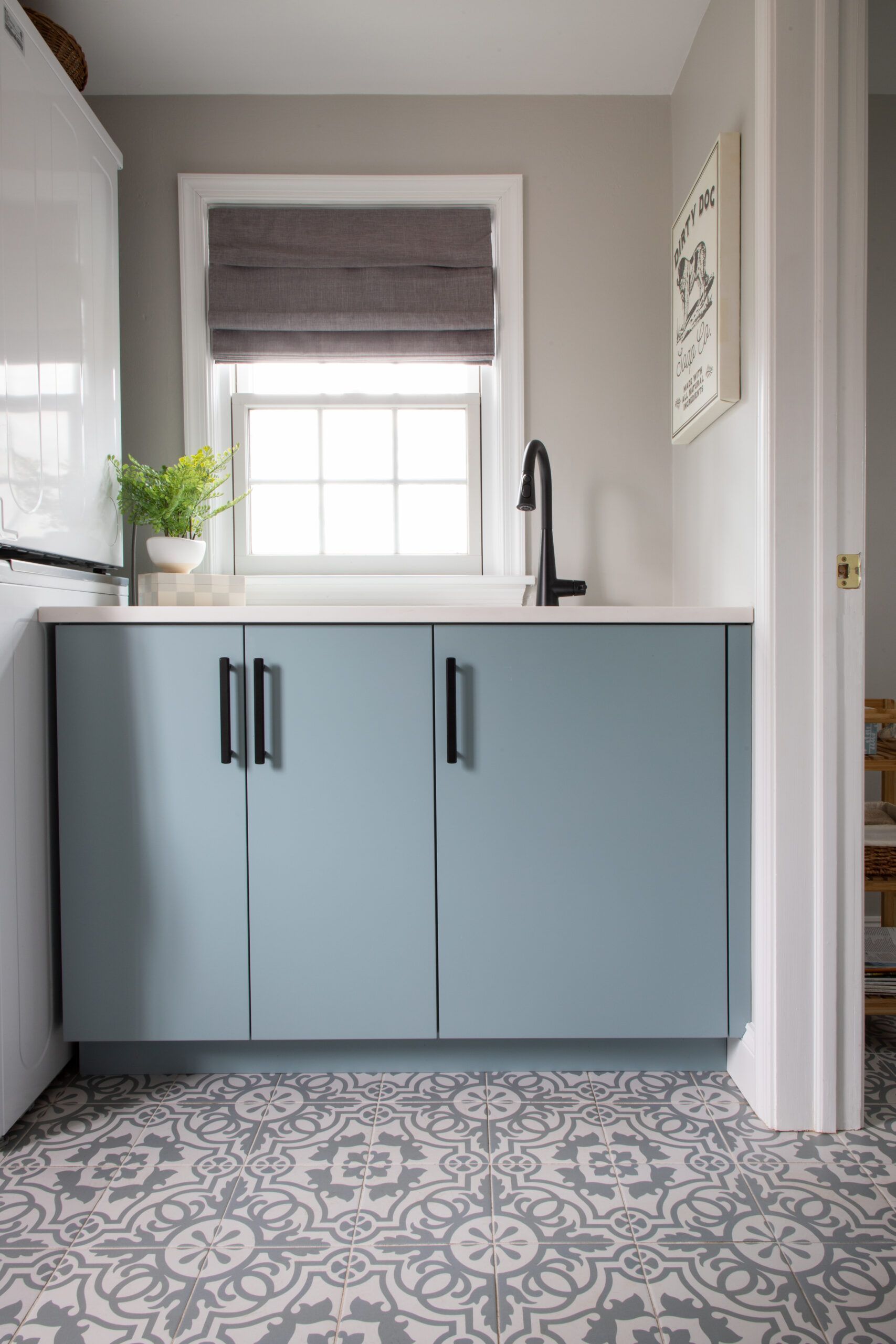 A laundry room with blue cabinets , a sink , and a window.