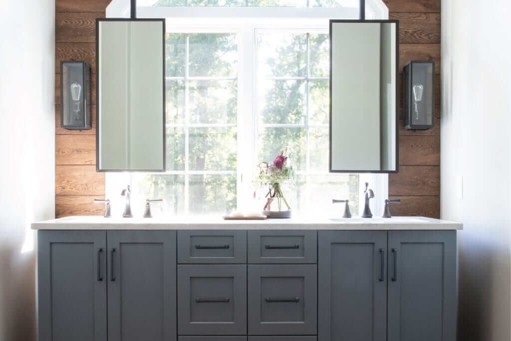 A bathroom with two sinks , two mirrors and a window.