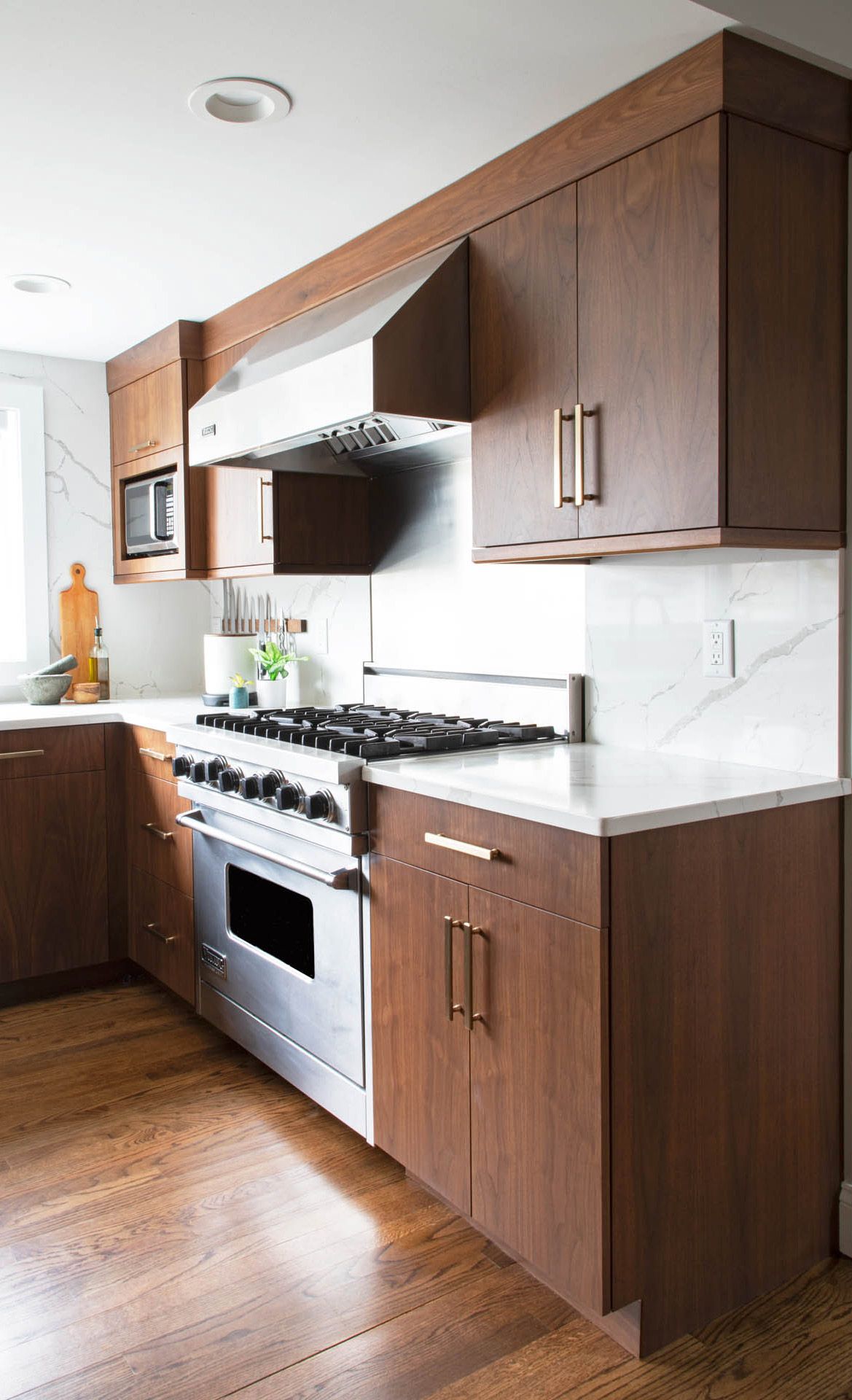 A modern kitchen featuring rich-toned wood cabinets, a stainless steel gas range, and a white marble backsplash.