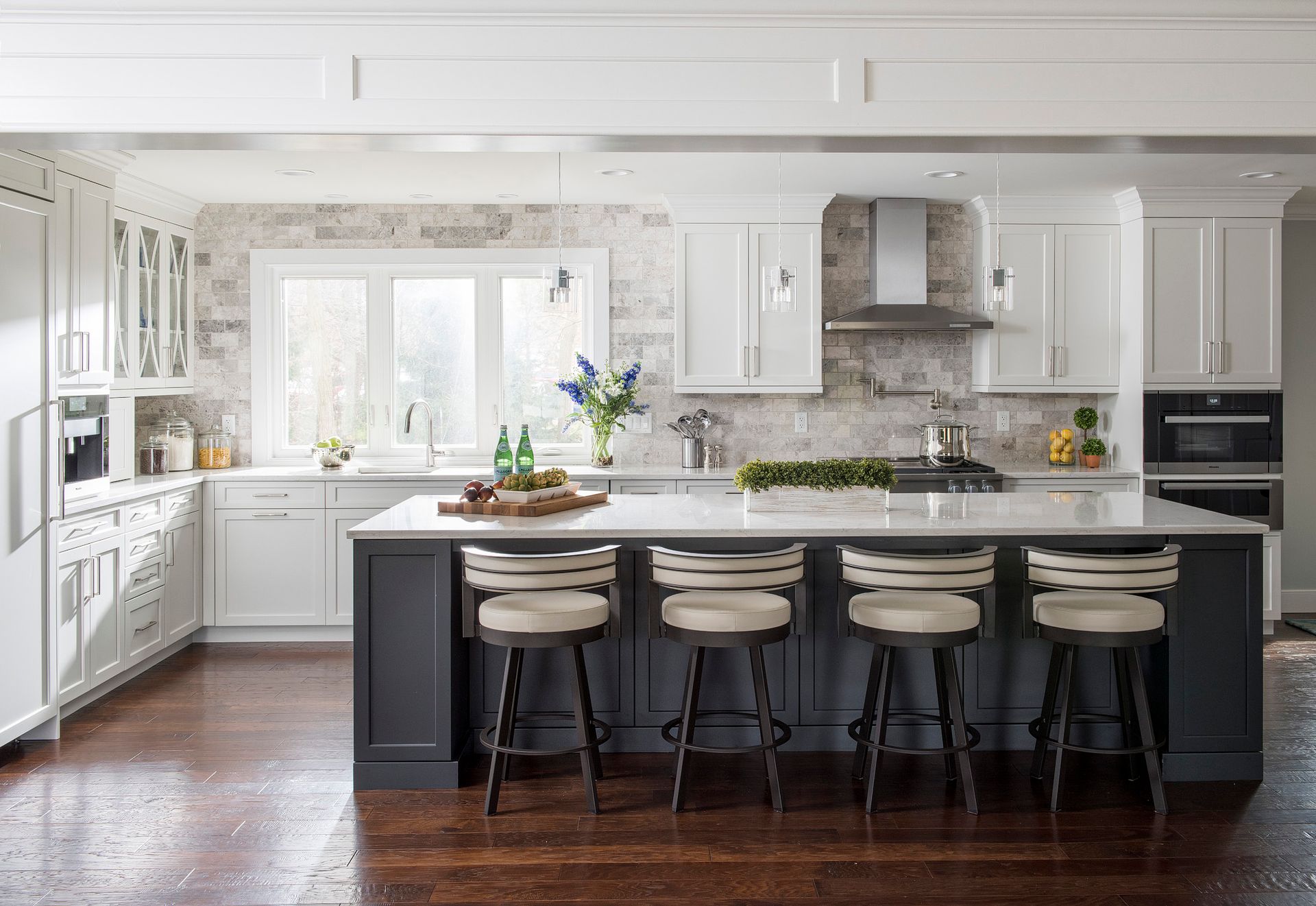A kitchen with white cabinets , a large island , and stools.