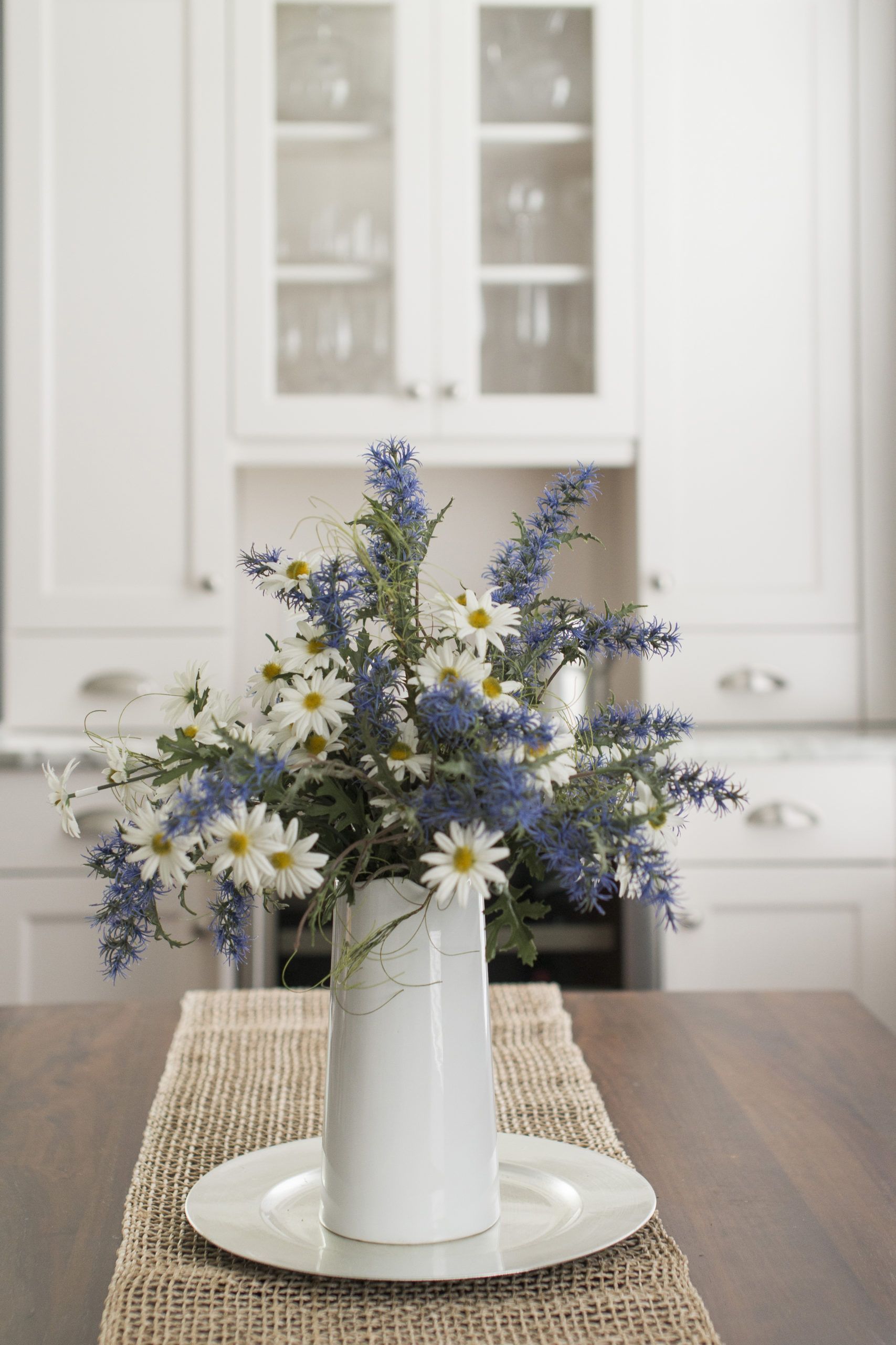 A vase filled with daisies and blue flowers is on a table.