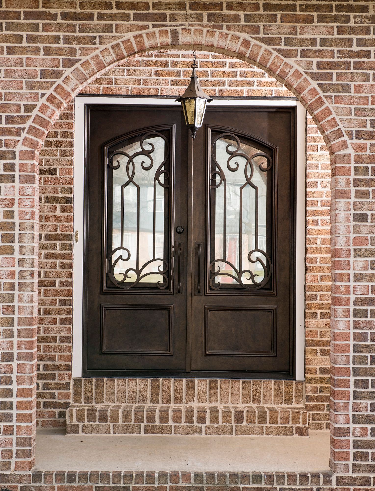 A double door with a wrought iron frame is on a brick wall.