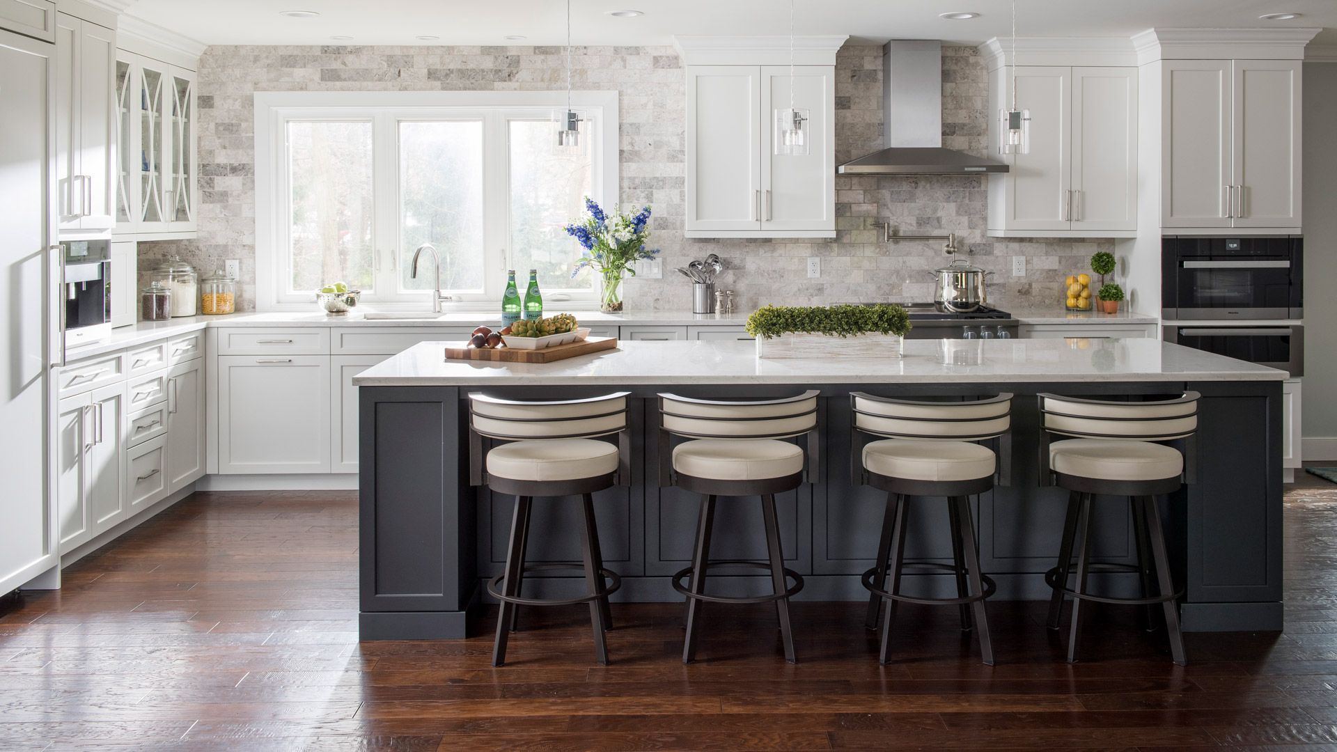 Gray kitchen range with hood, marble backsplash, and two windows.