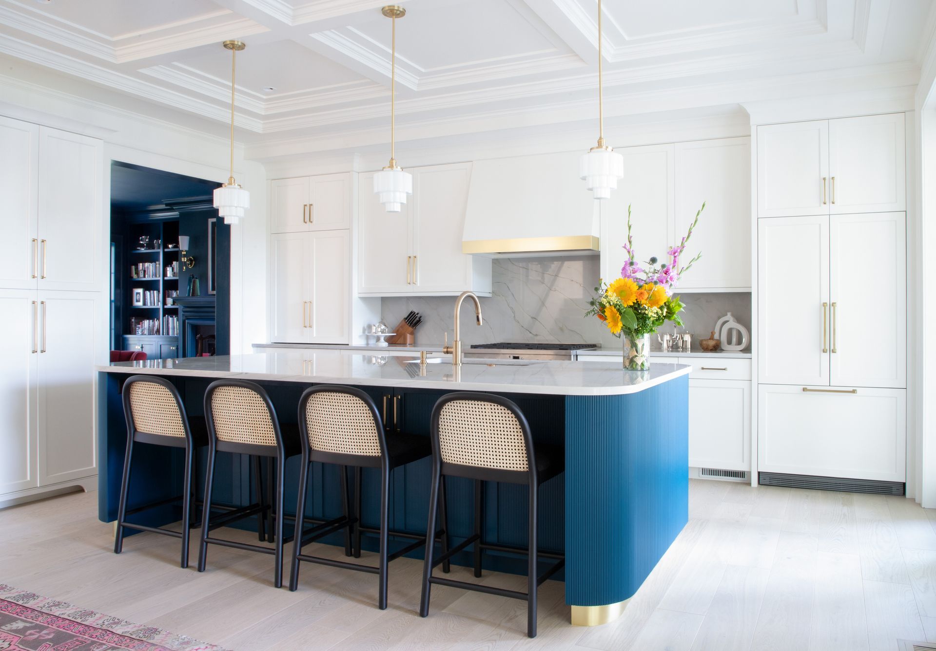 Elegant white kitchen with blue island, gold accents, and woven bar stools.