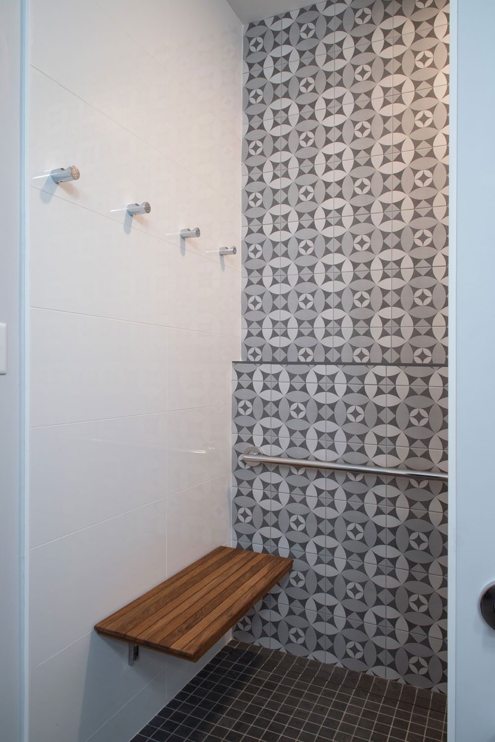 An ADA complaint bathroom  shower with a wooden bench and a patterned wall.