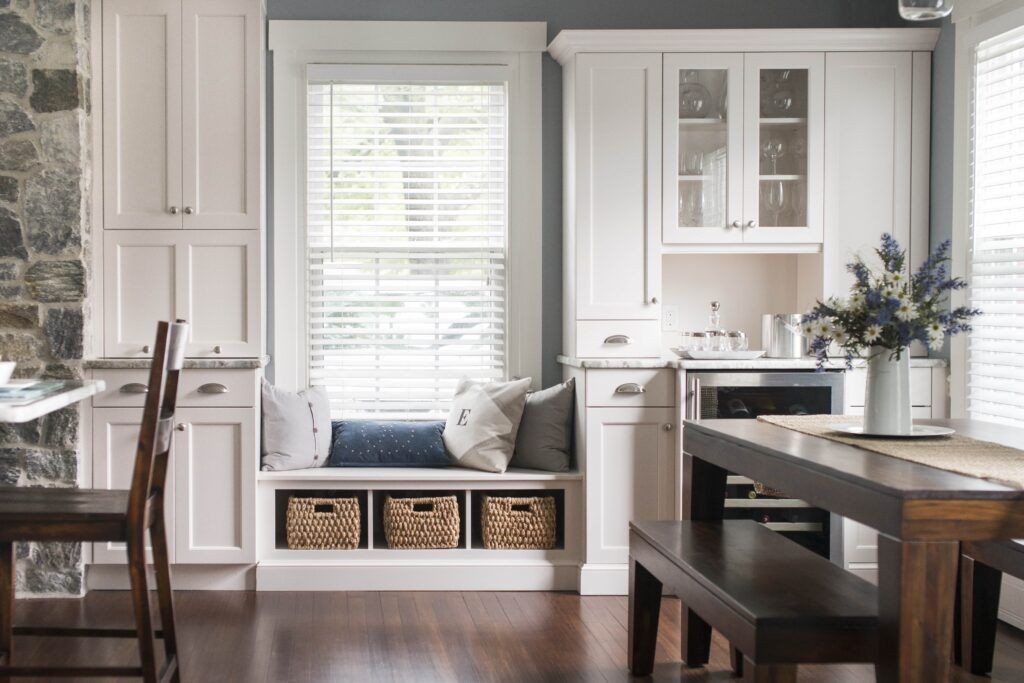 A kitchen with white cabinets , a bench , a table and chairs.