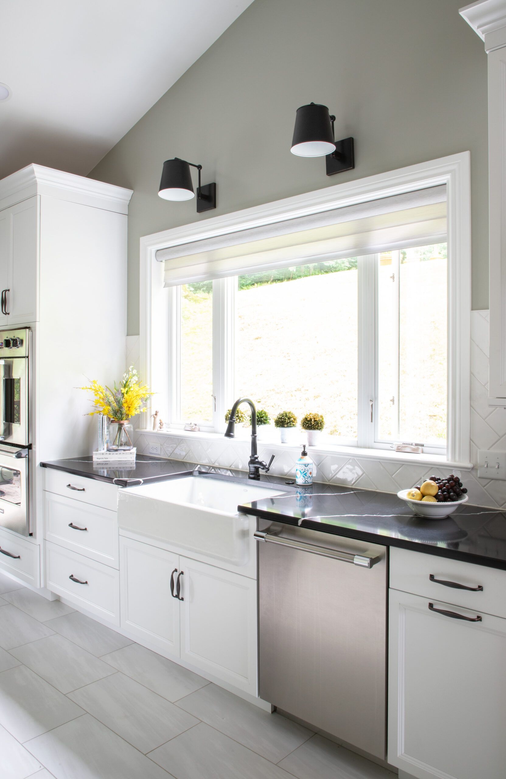 A kitchen with white cabinets , a sink , a dishwasher , and a window.