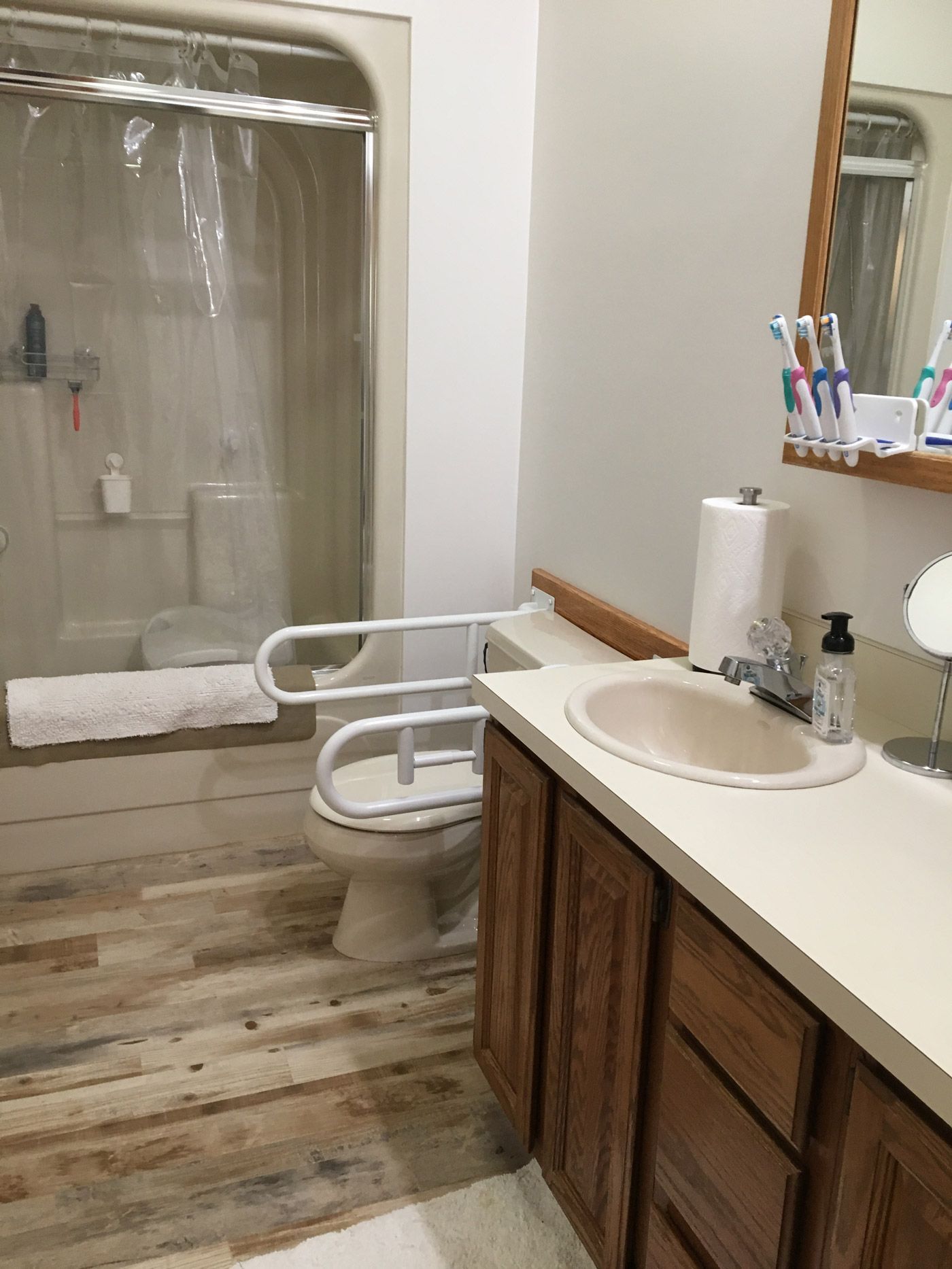 A bathroom with wood-look flooring, a vanity with a sink, and a toilet equipped with white safety support rails.