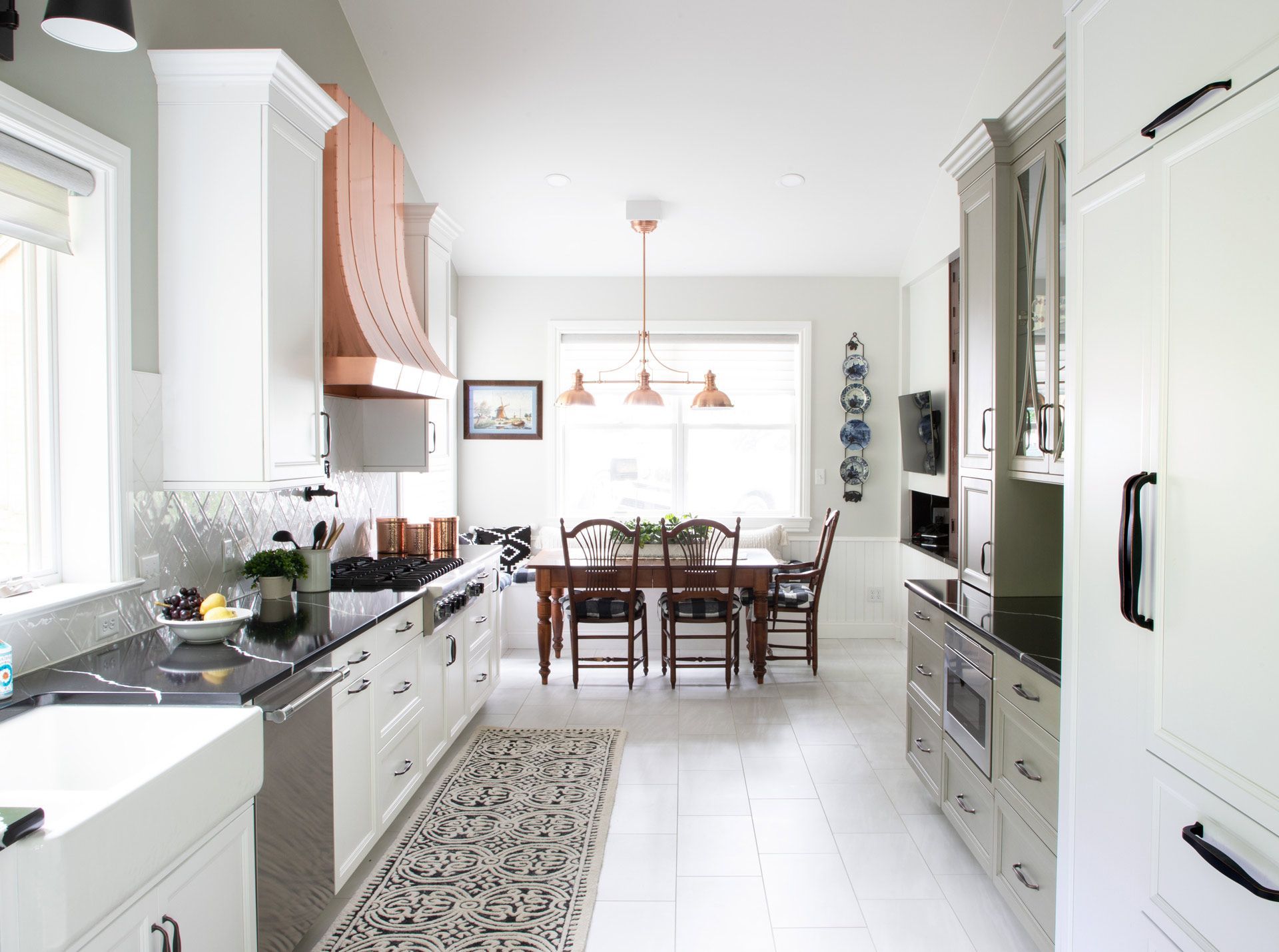 Bright white kitchen with dark counters, pendant lights, and a dining table in the background