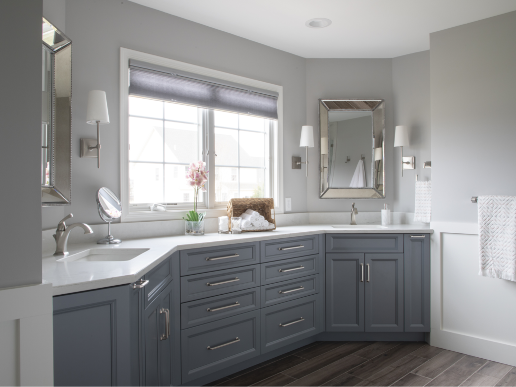 A bathroom with gray cabinets , a sink , a mirror and a window.