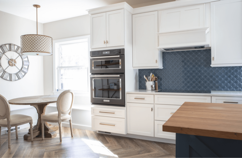 A kitchen with white cabinets , a clock on the wall , a table and chairs.