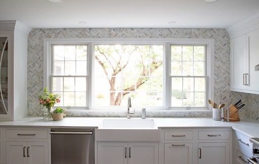 A kitchen with white cabinets , a sink , and a large window.