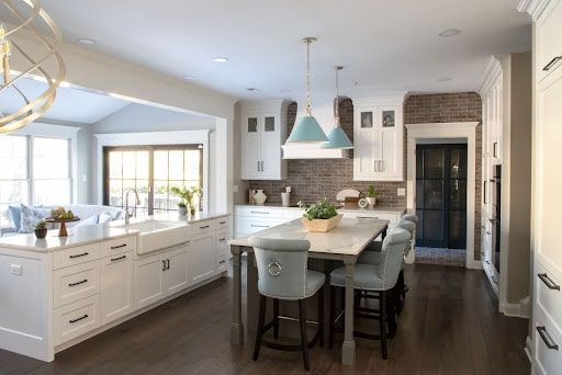 A kitchen with white cabinets , a large island , a table and chairs.