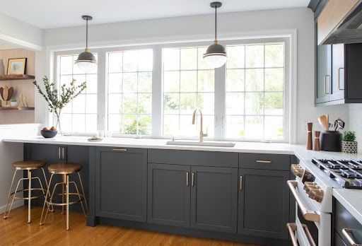 A kitchen with gray cabinets , a stove , a sink , and a large window.