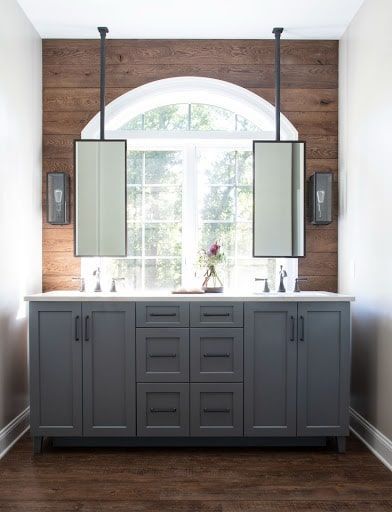 A bathroom with two sinks and two mirrors hanging from the ceiling.