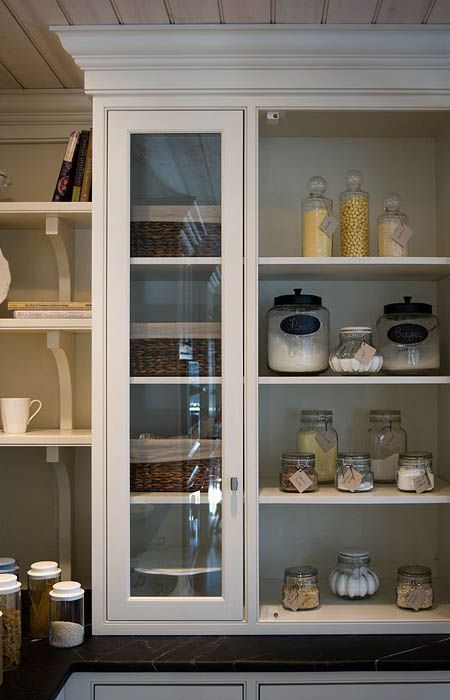 A pantry with a glass door and shelves filled with jars and baskets.