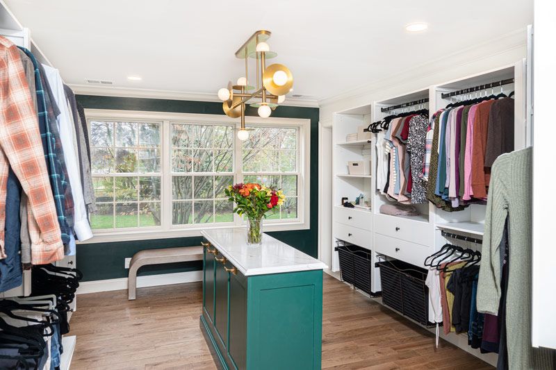 A walk in closet with lots of clothes and a large island in the middle.