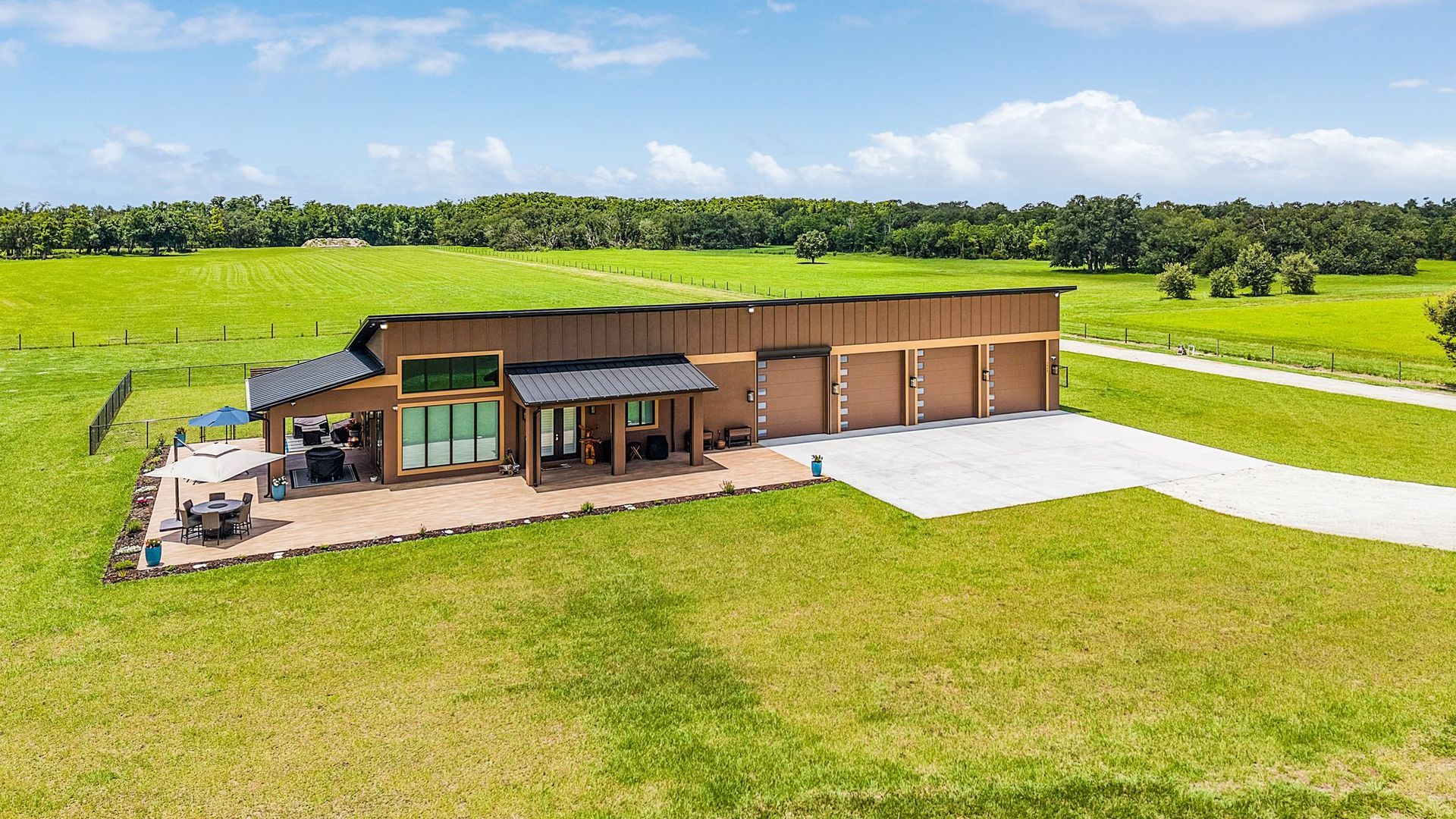 Modern brown house with attached garages on a grassy field with trees in the background.